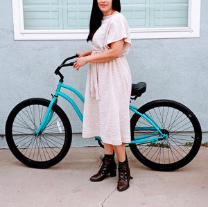 Powerful modestly dress women in a tunic dress holding a bicecle